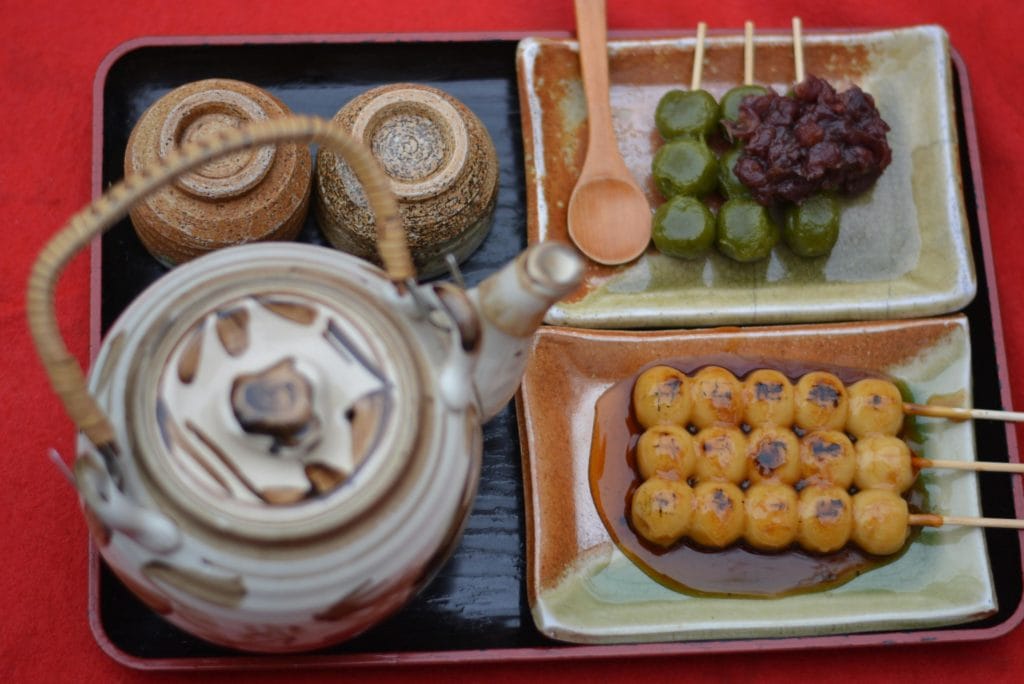 Traditional Japanese tea set with sweet dango skewers on a red tray, perfect for cultural food photography.